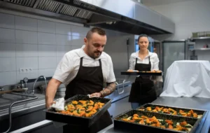 Male and female chefs placing trays of roasted vegetables onto a kitchen counter