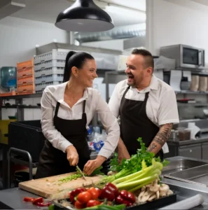 Two chefs laughing together while chopping vegetables in a commercial kitchen
