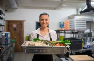 Female chef holding a tray of fresh vegetables in a professional kitchen
