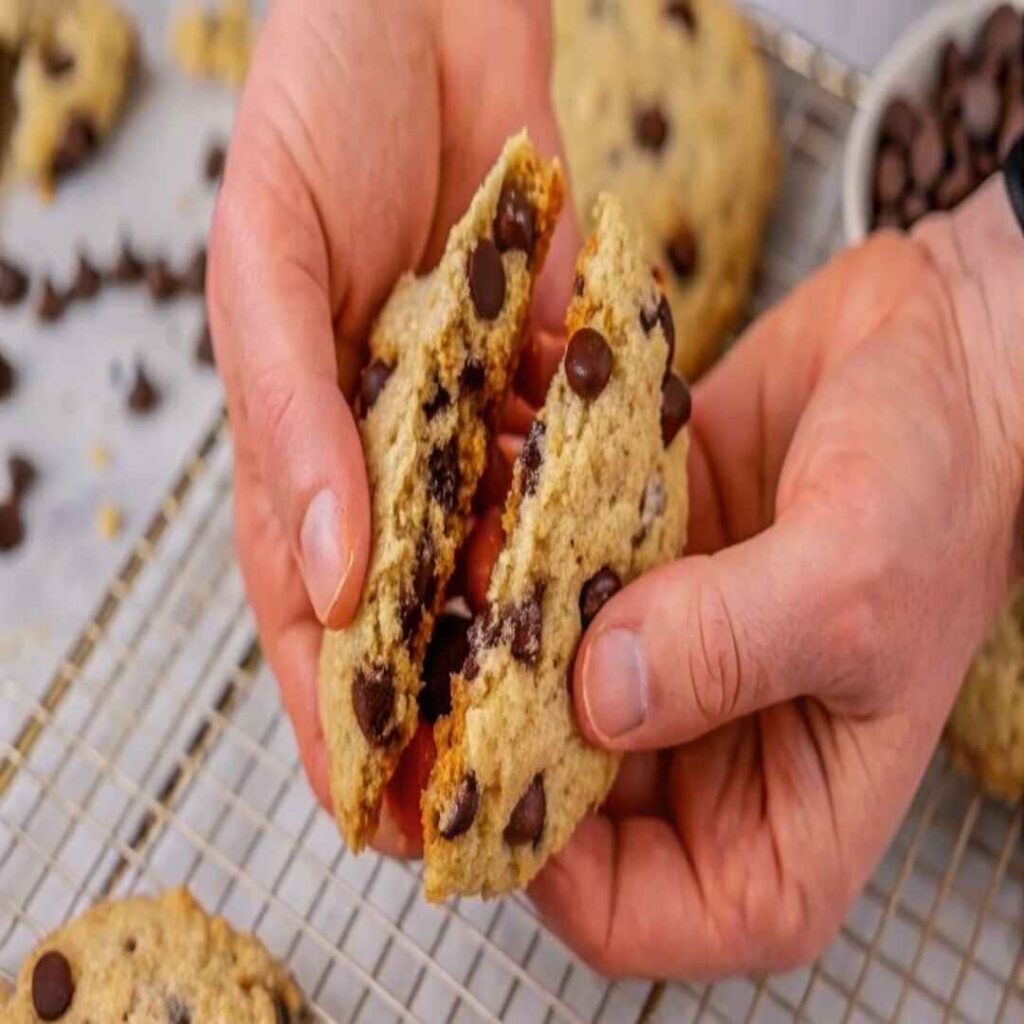 Hands breaking a gooey chocolate chip protein oatmeal cookie in half