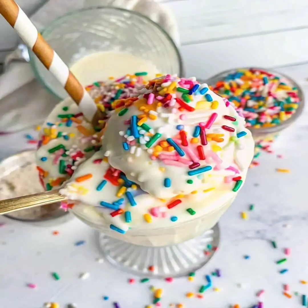 A spoonful of creamy vanilla protein shake topped with colorful rainbow sprinkles
