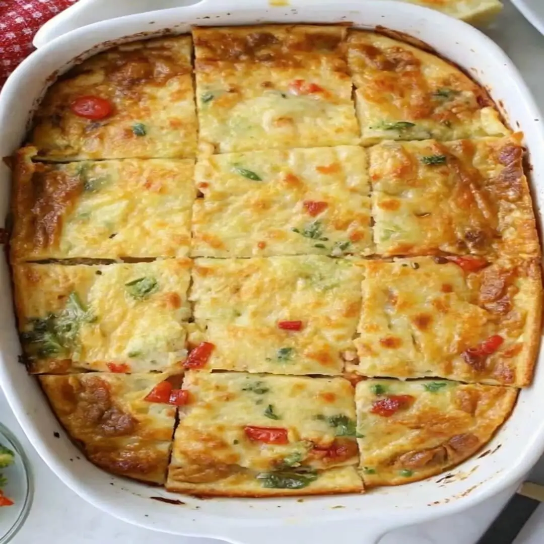 Top-down view of a baked egg casserole with sausage and vegetables, cut into squares