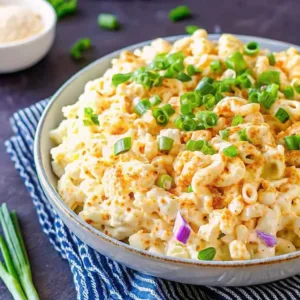 Close-up of macaroni salad with a thick creamy sauce, sprinkled with paprika and fresh green chives in a ceramic bowl.