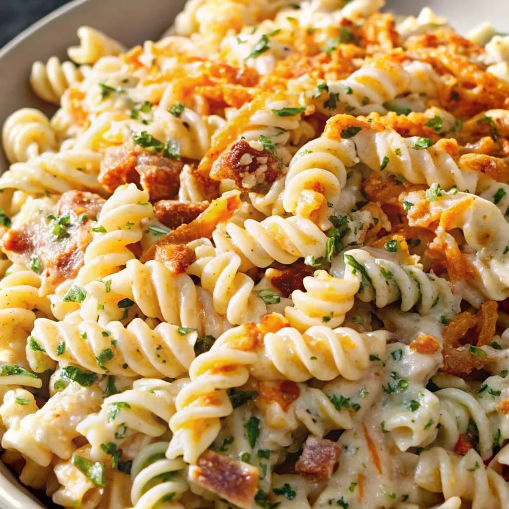 Spiral pasta salad featuring a generous amount of bacon crumbles and fresh green herbs in a creamy dressing.