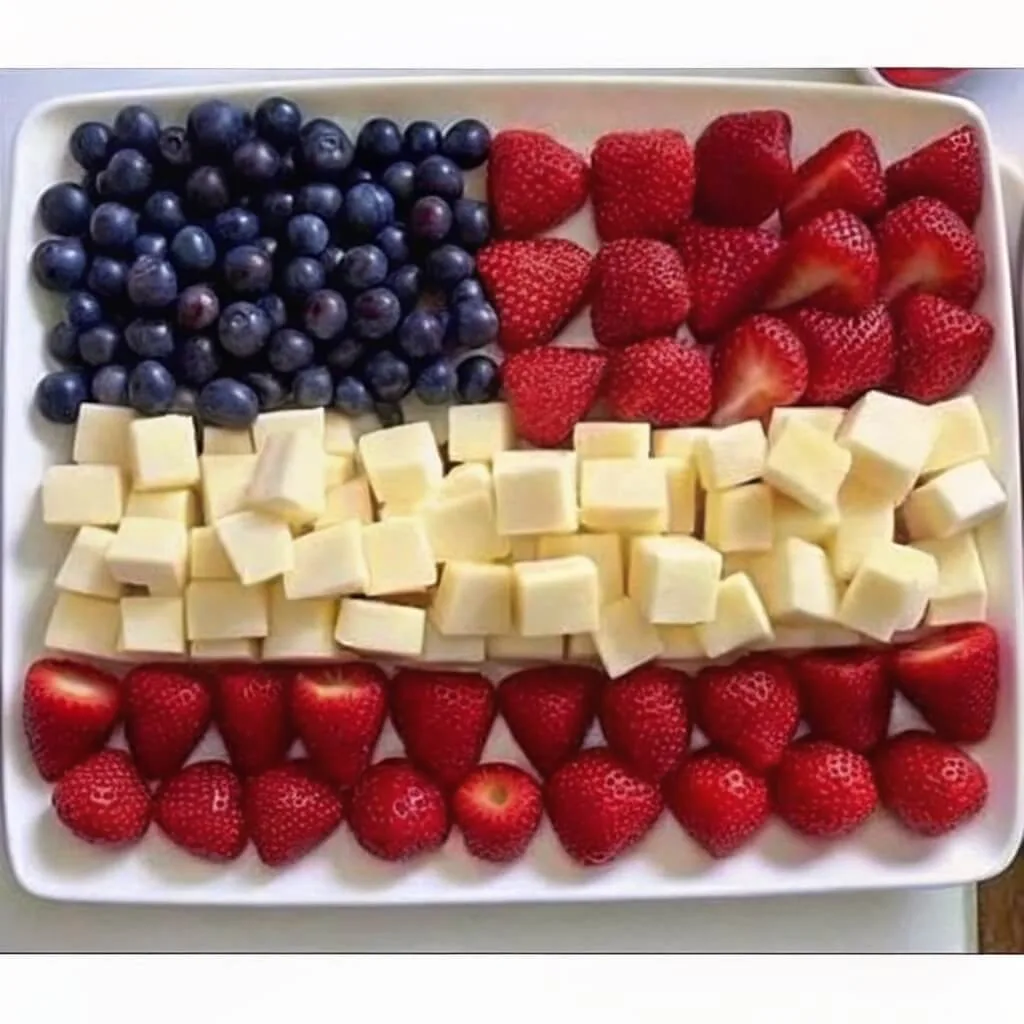 A top-down view of a white tray with blueberries in the corner and alternating horizontal rows of strawberries and cheese cubes.