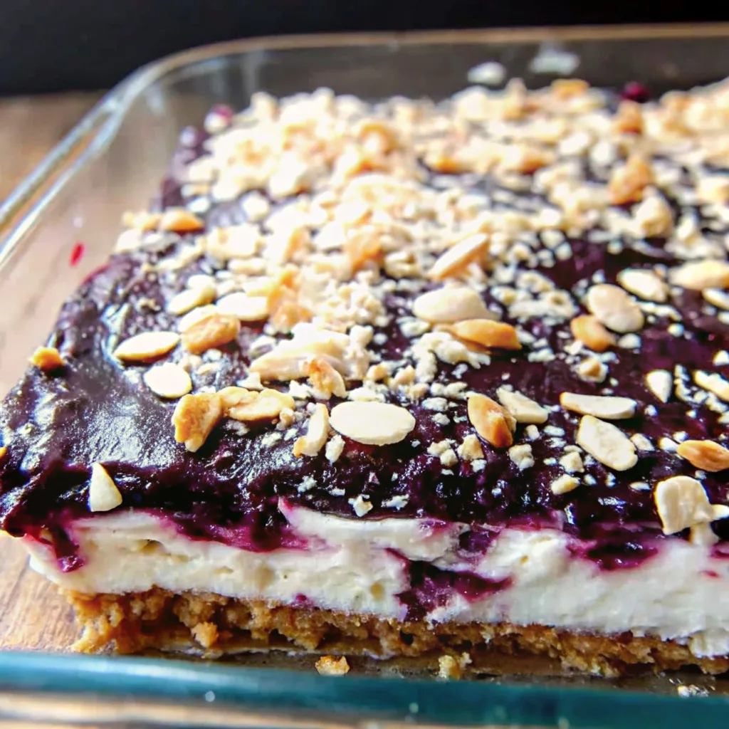 Close-up of a layered blueberry lush dessert in a clear baking dish, highlighting the thick blueberry compote and crushed nuts on top.