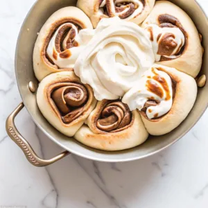Pull-apart cinnamon rolls arranged in a circular flower pattern in a silver pan with a large swirl of white frosting in the center.
