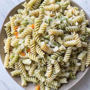 Spinach and plain rotini pasta tossed with carrots and light creamy dressing on a rustic ceramic plate.