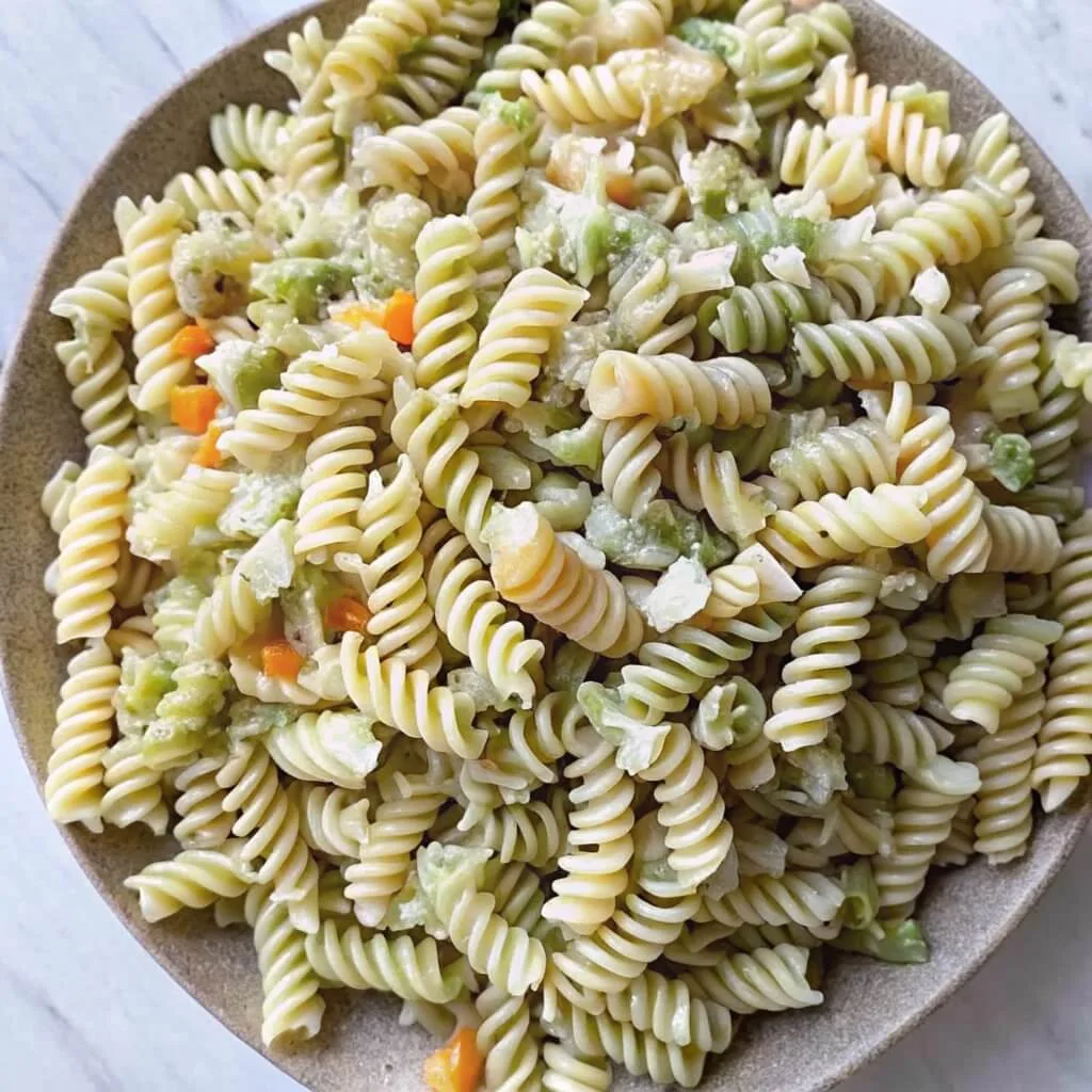 Spinach and plain rotini pasta tossed with carrots and light creamy dressing on a rustic ceramic plate.