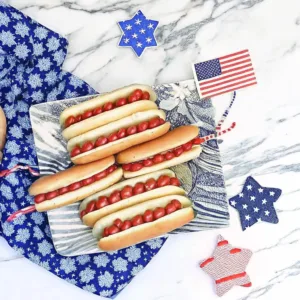 A top-down view of hot dogs on a decorative plate surrounded by patriotic star-shaped ornaments and a small flag.