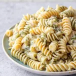 Detailed view of cooked rotini pasta with visible bits of green herbs and garlic in a creamy sauce.
