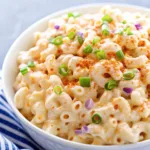 Detailed view of elbow macaroni salad showing the blend of creamy sauce, paprika, and fresh green onion rings.