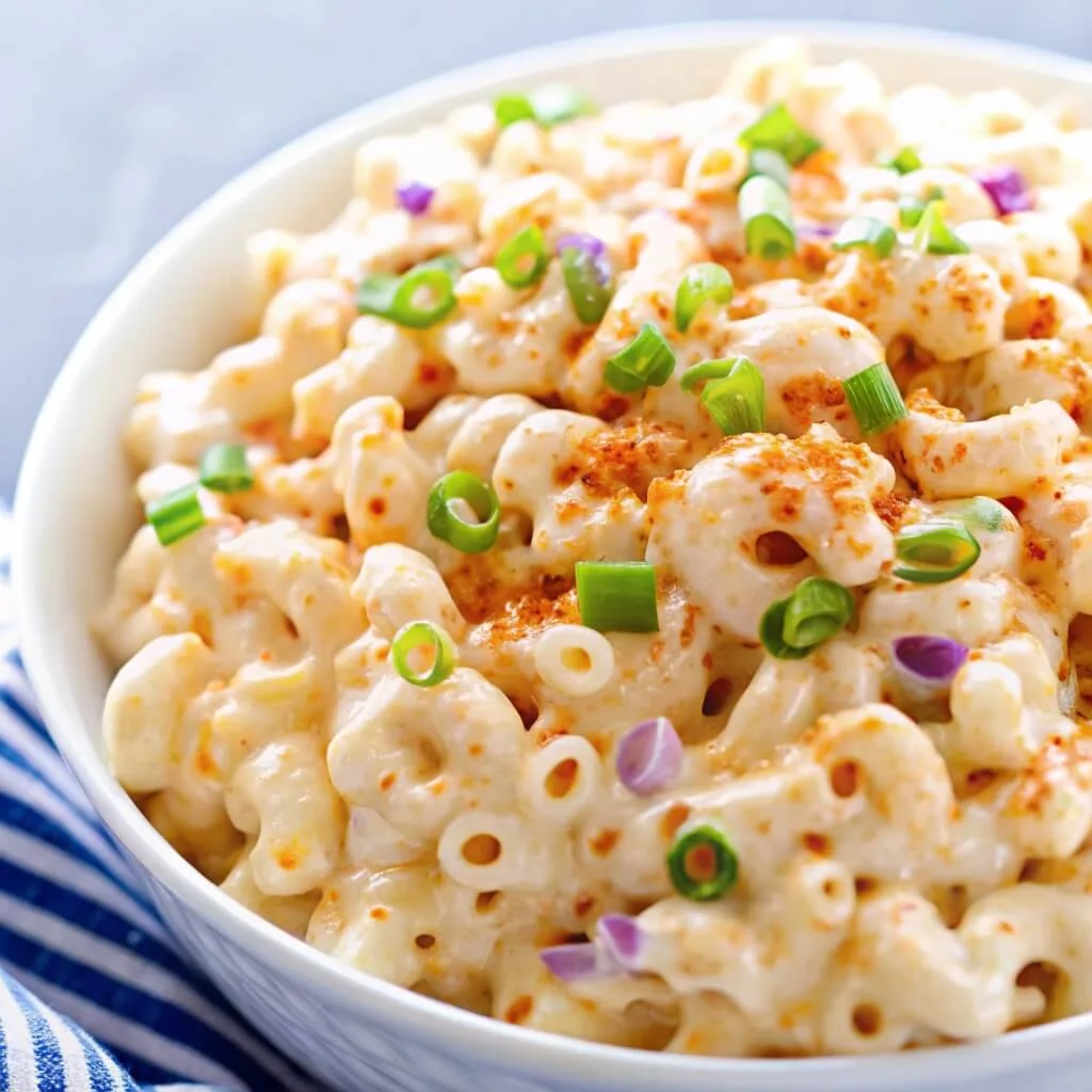 Detailed view of elbow macaroni salad showing the blend of creamy sauce, paprika, and fresh green onion rings.