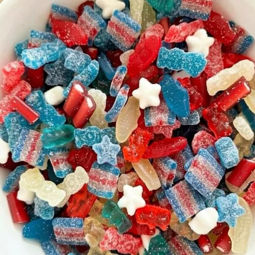 Top down view of a white bowl filled with a 4th of July candy salad containing red white and blue gummy bears, sour belts, Swedish fish, and star candies.