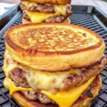 A close-up of a stacked breakfast sandwich featuring two sausage patties, melted cheddar cheese, and a fried egg between two thick, golden-brown pancakes.