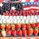 A wooden tray arranged as an American flag using blackberries, raspberries, strawberries, and yogurt-covered pretzels.