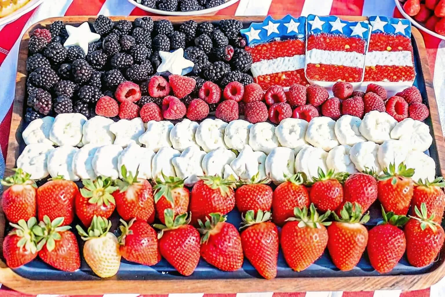 A wooden tray arranged as an American flag using blackberries, raspberries, strawberries, and yogurt-covered pretzels.