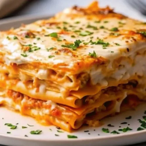 Side view of a slice of layered lasagna with melted cheese, meat sauce, and fresh parsley on a white plate.