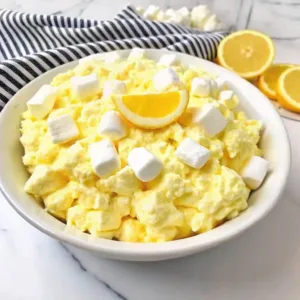 Classic Lemon Fluff Salad 4 Close up of creamy pale yellow lemon fluff salad topped with mini marshmallows and a fresh lemon slice.