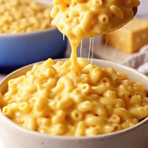 The Ultimate Simple Creamy Macaroni and Cheese 4 A golden spoon scooping creamy homemade macaroni and cheese from a bowl with a long melted cheese pull.