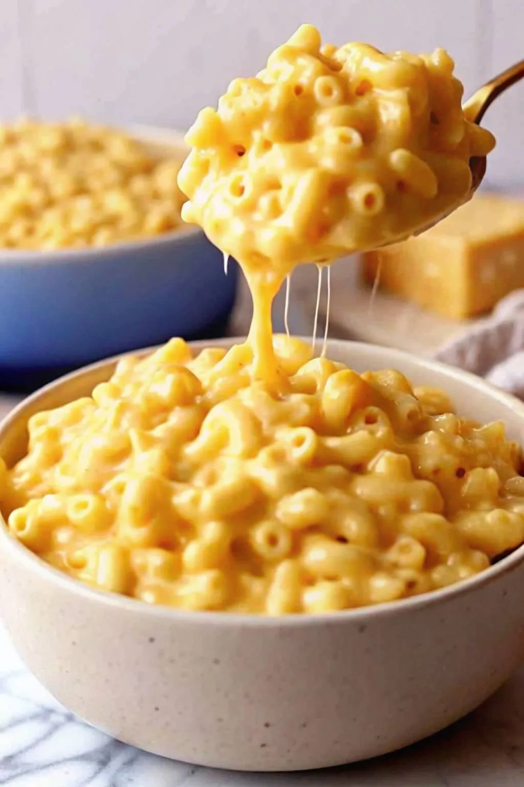 The Ultimate Simple Creamy Macaroni and Cheese 3 A golden spoon scooping creamy homemade macaroni and cheese from a bowl with a long melted cheese pull.