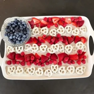 Festive Berry Flag Platter 3 An overhead view of a 4th of July charcuterie board shaped like an American flag with rows of strawberries, raspberries, yogurt covered pretzels, and a bowl of blueberries.