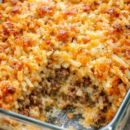 A glass baking dish filled with a cheesy hamburger hashbrown casserole, with a portion removed showing the layers of seasoned ground beef and crispy shredded potatoes.