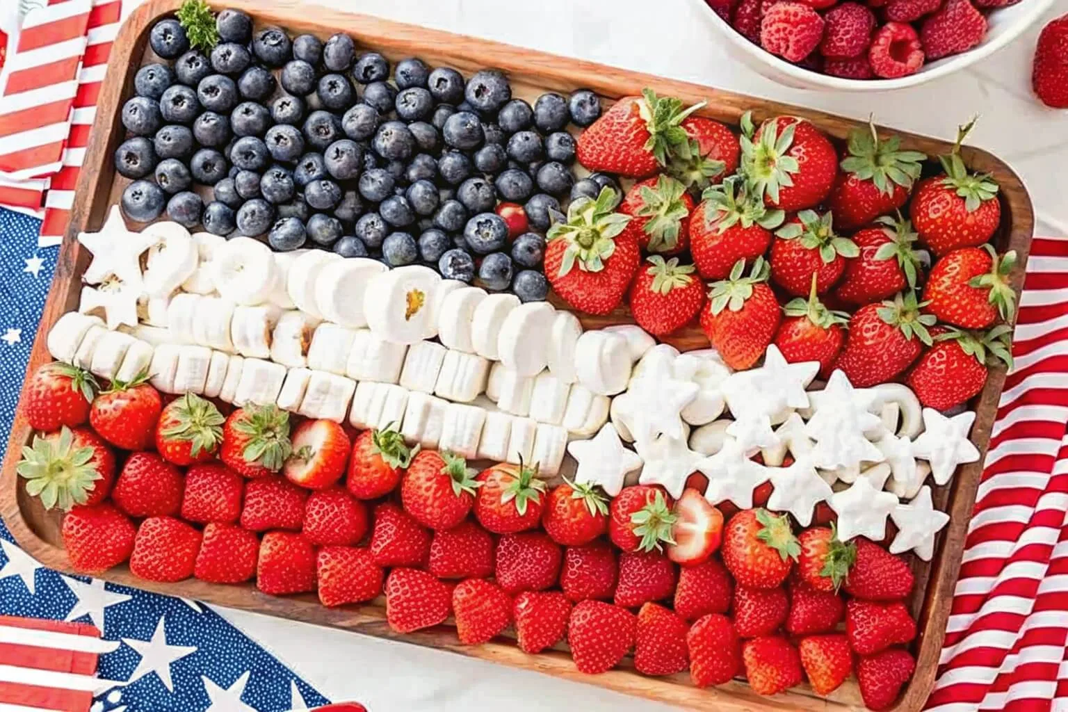 A wooden board featuring an American flag design made of blueberries, strawberries, and white marshmallows.
