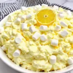Overhead view of a white bowl filled with creamy lemon jello fluff dessert salad and marshmallows.