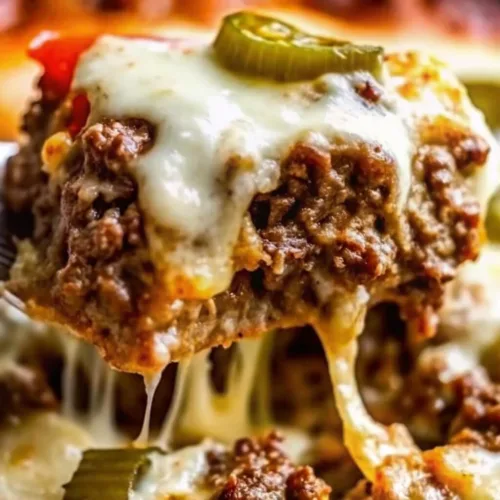 A server scooping a cheesy keto ground beef bake topped with jalapeno slices and a long cheese pull.