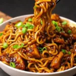 A detailed close-up of savory stir-fry noodles mixed with tender chicken pieces and topped with freshly sliced green onions.