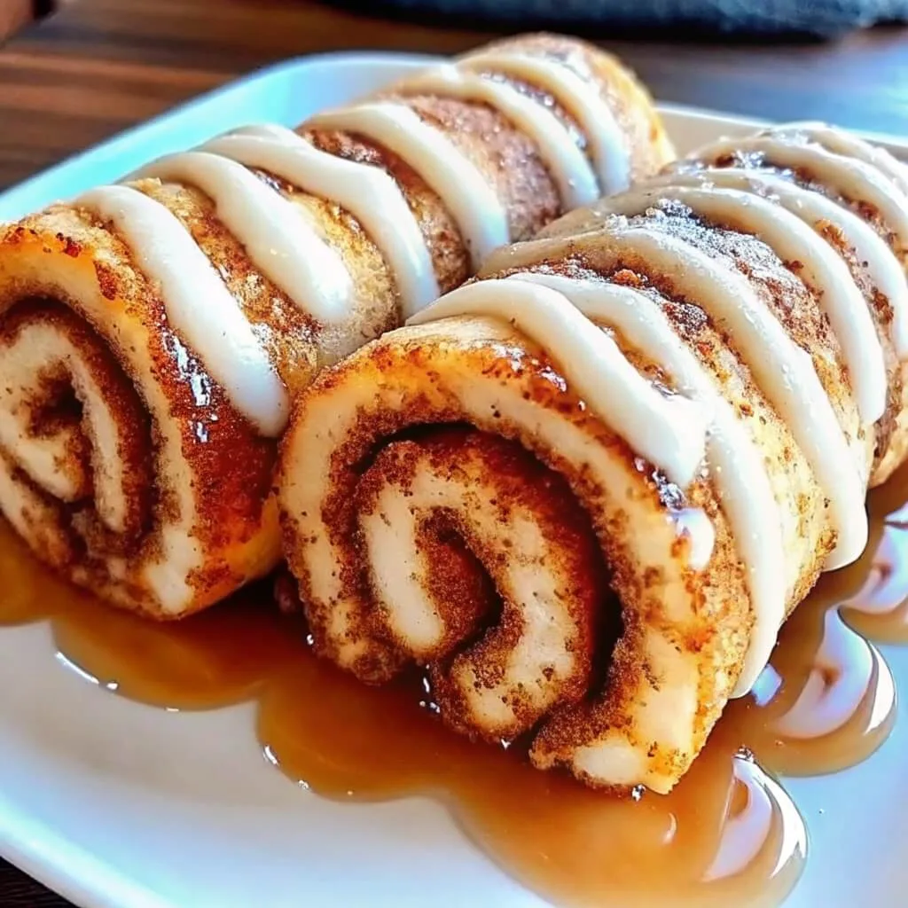 Easy Cinnamon Roll French Toast Roll-Ups 2 Angled food photography of two baked crescent roll cinnamon logs with a white powdered sugar icing drizzle and brown sugar filling.