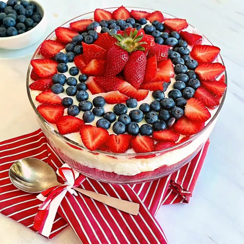 A top-down view of a trifle bowl decorated with rings of blueberries and strawberries, placed on a red and white striped napkin.