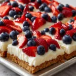 An angled close up shot of layered cream cheese fruit bars with a graham cracker crust and mixed berry topping on a metal tray.