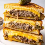 A tall stack of three patty melt sandwich halves showing thick layers of beef patty and melted cheese topped with a pickle.