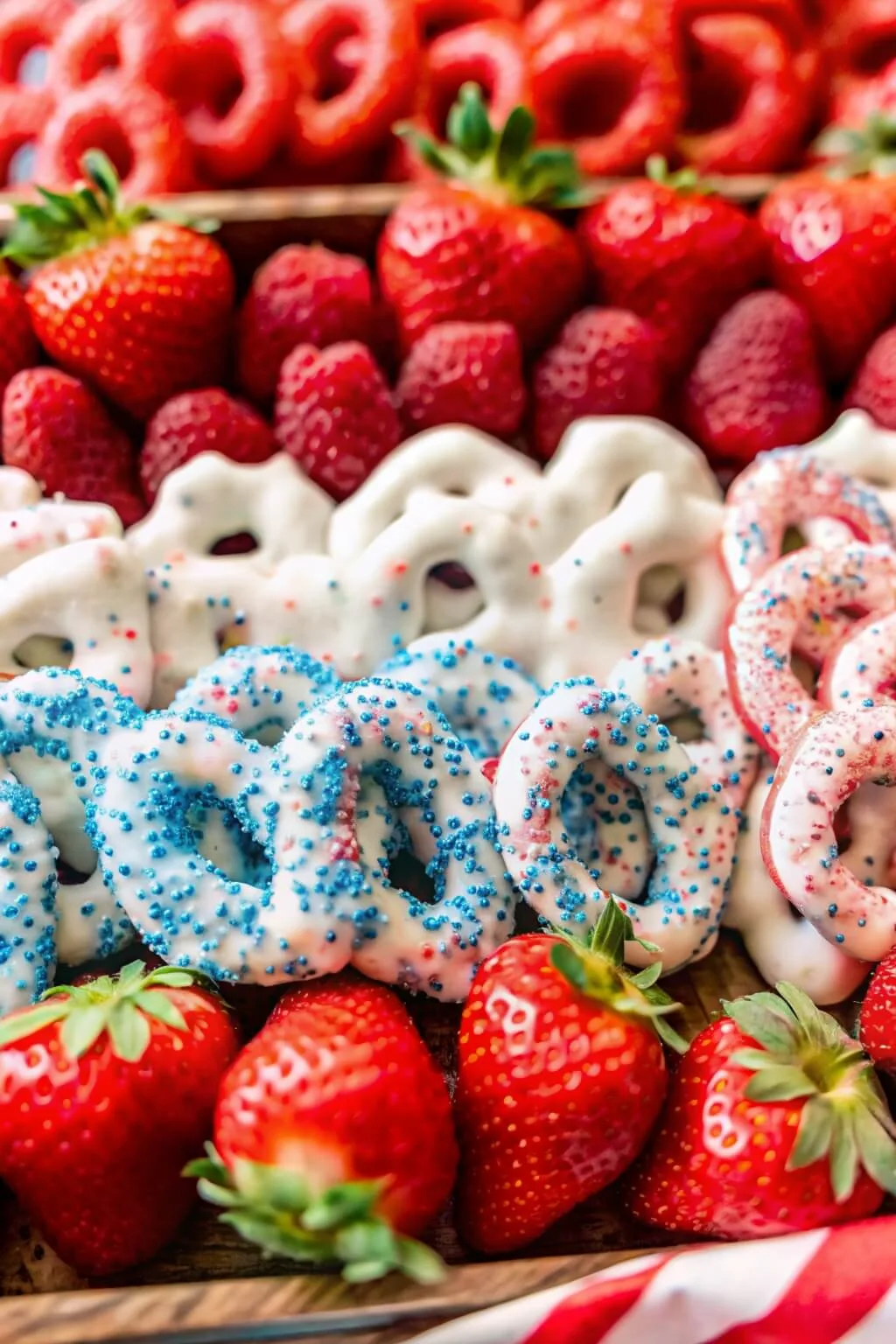 A close-up of red and blue sprinkled yogurt pretzels layered between fresh strawberries and raspberries.