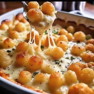 A spoonful of crispy tater tots and melted cheese sauce being lifted from a baking pan.