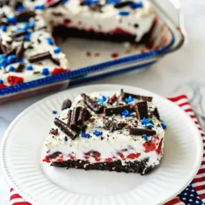 A single serving of red velvet patriotic cake on a white plate, featuring chocolate curls and blue star sprinkles.