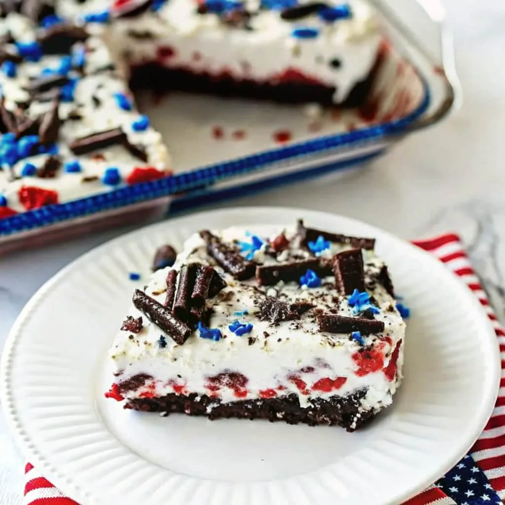A single serving of red velvet patriotic cake on a white plate, featuring chocolate curls and blue star sprinkles.