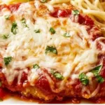 Baked chicken parmesan served with marinara sauce and fresh basil on a plate.